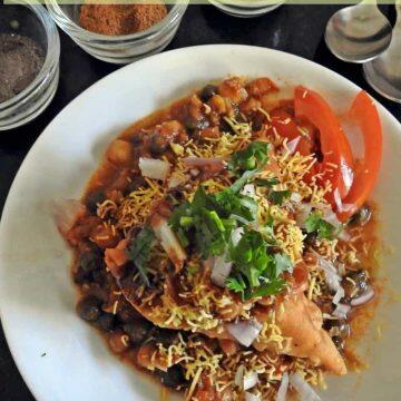 Samosa Chaat is mashed samosa topped with peas or chole masala and topped with tangy chutneys, sev, onion and tomatoes if you wish.